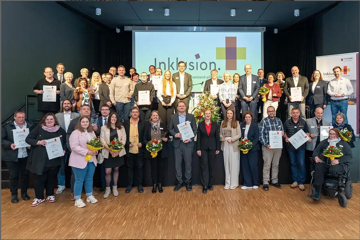 Gruppe von Menschen, die mit Auszeichnungen und Blumensträußen auf und unter der Bühne stehen. 