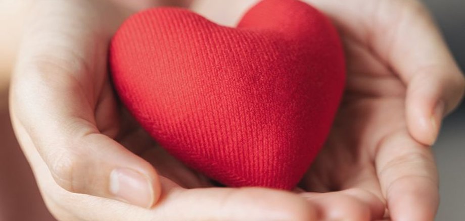 Zwei ineinander verschränkte Hände mit den Innenflächen nach oben, darin liegt ein rotes Herz, passend zum Titel Gesundes Herz- wie Frauen ihre Herzen stärken.