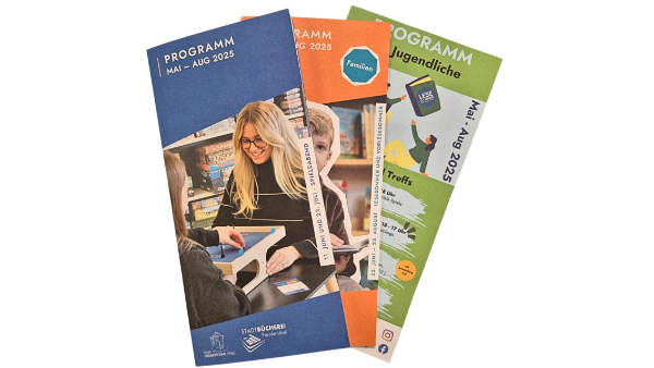 Die drei Veranstaltungsprogramme für Erwachsene, Familien und Jugendliche liegen aufgefächert vor weißem Hintergrund.