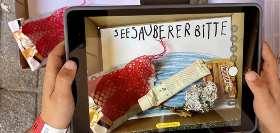 Mit Tablet Postkarten fotografieren Hände halten ein Tablet, mit dem gerade ein selbst gemaltes Bild fotografiert wird.