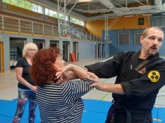 Foto zeigt drei Personen in der Sporthalle und der vordere greift eine Person am Ellenbogen an.